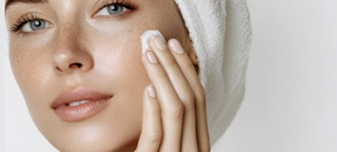 Mujer con toalla en el cabello aplicando crema facial sobre piel limpia